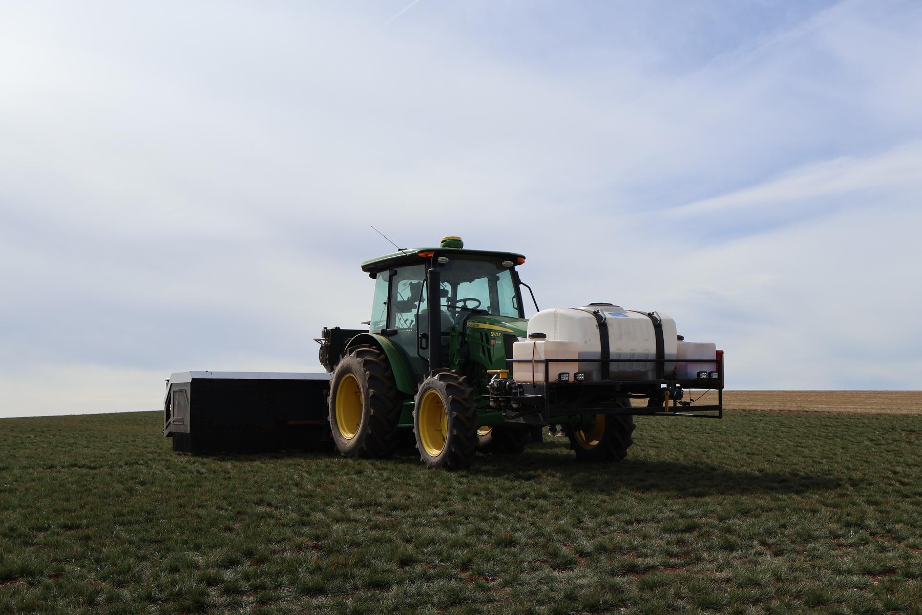 Atlas in a grass field, white tank on the front of the tractor and the implement behind.