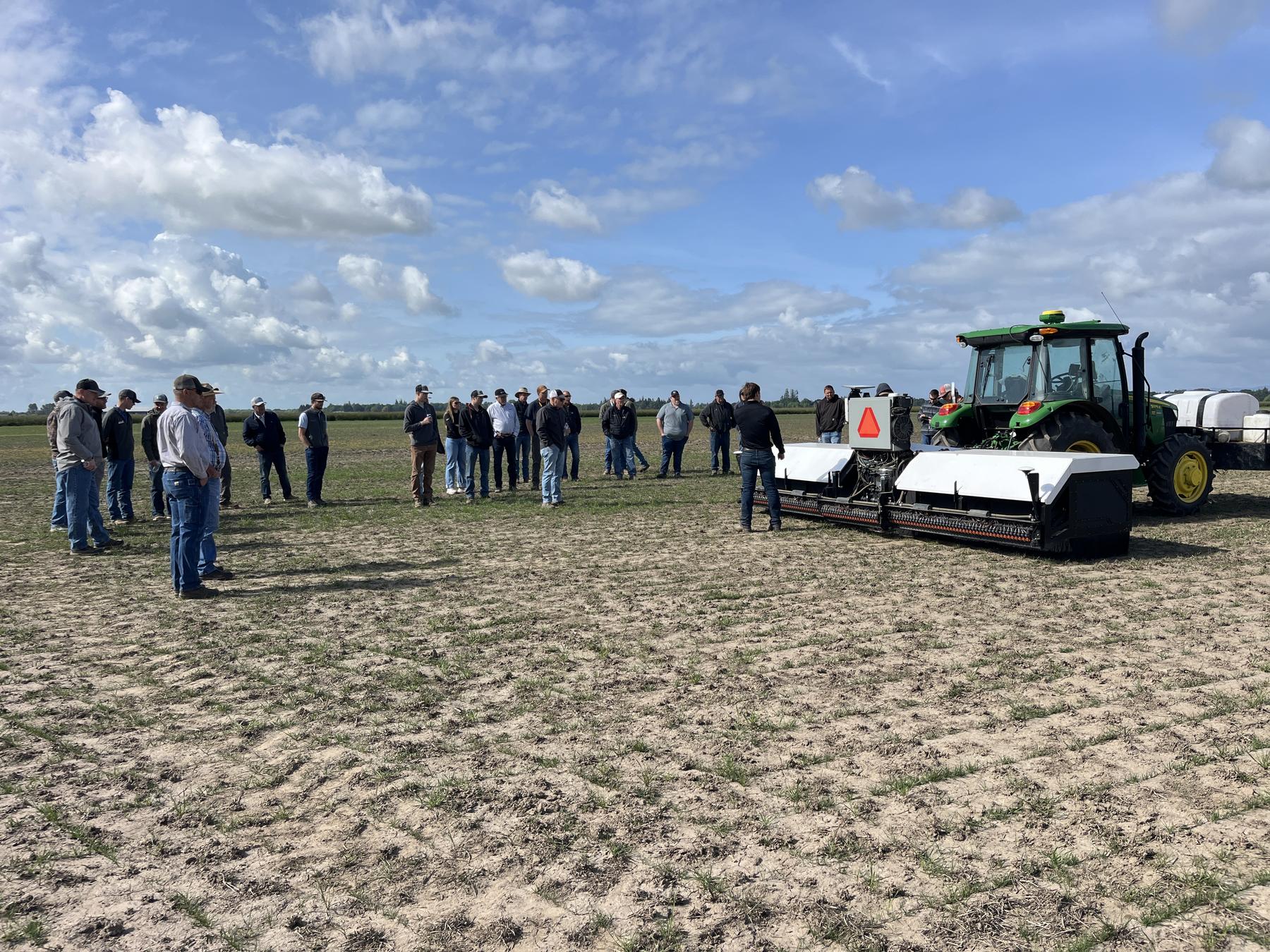People standing in a field beside Atlas and a tractor.