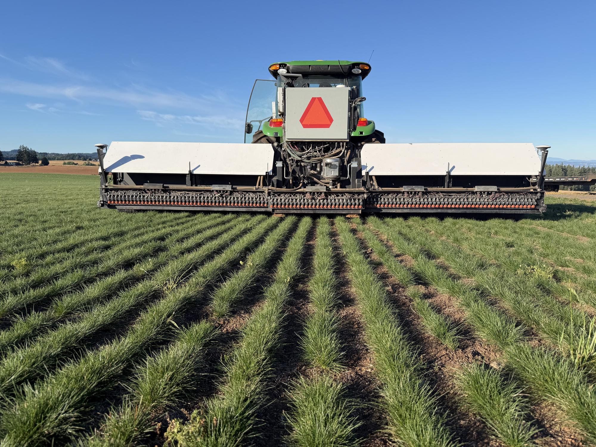 Atlas sprayer working a grass field behind a tractor.